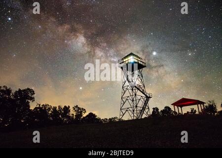 Il centro della Via Lattea ruscella dietro la spornosa Torre dei Vigili del fuoco, illuminata dall'interno, in una notte di prima estate nella Foresta Statale di Seneca Foto Stock