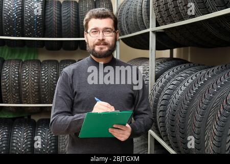 Venditore con appunti vicino pneumatici su scaffali in negozio di automobili Foto Stock