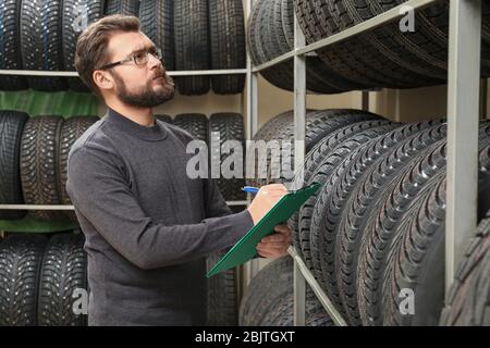 Venditore con appunti vicino pneumatici su scaffali in negozio di automobili Foto Stock