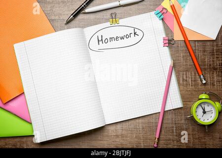 Copybook con parola 'Homework' e cancelleria su sfondo di legno, vista dall'alto Foto Stock