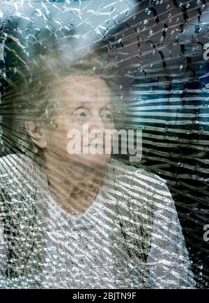Donna di novanta anni che guarda fuori dalla finestra cracked in un giorno piovoso. Isolamento di sé, solitudine, coronavirus, concetto di distanza sociale... Foto Stock