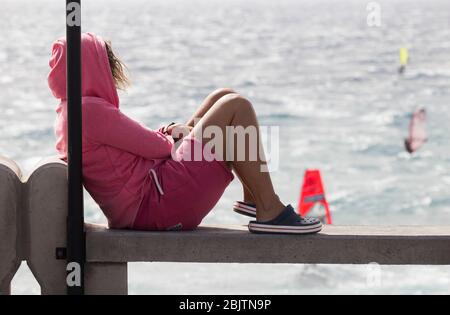 Donna con felpa con cappuccio rosa e cocchi che guarda i windsurf a Pozo Izquierdo a Gran Canaria, Isole Canarie, Spagna Foto Stock