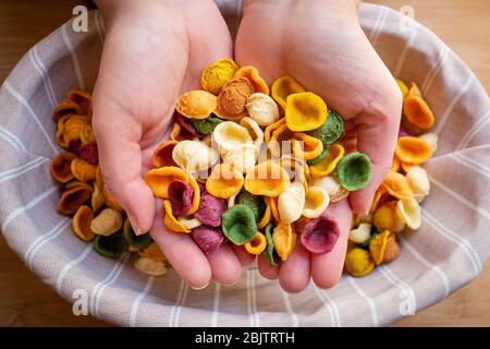 Le mani femminili tengono le orecchiette colorate fatte a mano sulla pasta fresca. Cucina tradizionale pugliese, Italia Foto Stock
