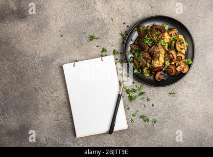 Stufato di manzo fatto in casa con funghi e un contorno di lenticchie su un piatto nero e notebook per le ricette. Spazio di copia della vista superiore Foto Stock