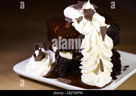 Una torta al cioccolato in stile brownie servita a Barrington, Nuova Scozia, Canada. Il dessert è condito con panna montata e cioccolato in fiocchi. Foto Stock