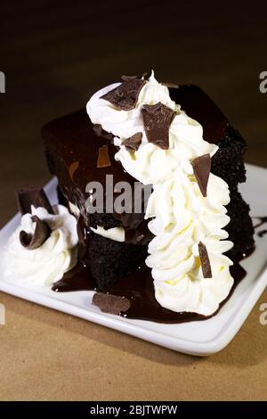 Una torta al cioccolato in stile brownie servita a Barrington, Nuova Scozia, Canada. Il dessert è condito con panna montata e cioccolato in fiocchi. Foto Stock