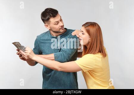 Donna che cerca di prendere soldi dal marito per lo shopping contro sfondo chiaro Foto Stock