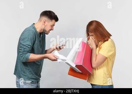 L'uomo arrabbiato sgridava la moglie che ha speso un sacco di soldi per lo shopping, contro sfondo chiaro Foto Stock