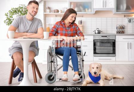 Cane da servizio sdraiato sul pavimento vicino alla donna in sedia a rotelle al chiuso Foto Stock