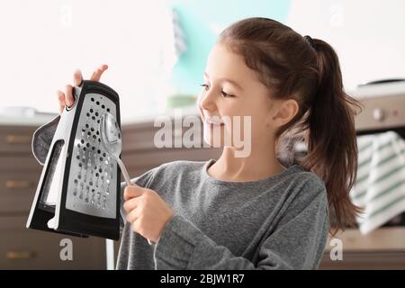 Ragazza carina che suona musica con grater e cucchiaio in cucina Foto Stock