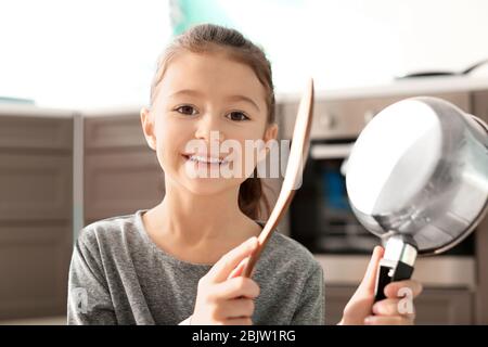 Ragazza carina che suona musica con cucchiaio e pentola al chiuso Foto Stock