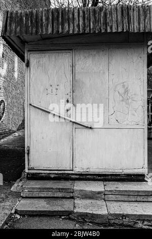 Foto in bianco e nero di vecchio stalla di laboratorio di scarpe con porta chiusa e muro grungo. Pareti dipinte e macchiate di retro e sporche Foto Stock