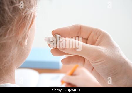 Donna che inserisce l'apparecchio acustico nell'orecchio della bambina, primo piano Foto Stock