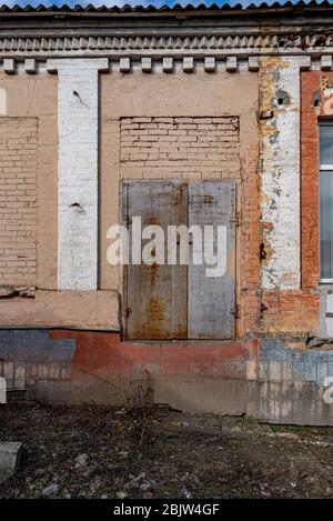 Grunge muro di mattoni di edificio abbandonato con bianche colonne false e arrugginito metallo porta chiusa. La facciata della casa ha bisogno di ricostruzione Foto Stock