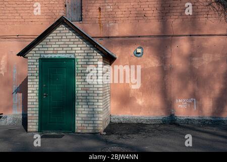 Porta verde scuro e tetto a forma di triangolo di portico in edificio retrò con grunge stucco muro e iscrizione "uscita al ponte" in lingua russa. Grung Foto Stock