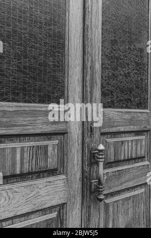 Foto in bianco e nero di pannelli di legno a doppia porta con finestre rettangolari e cornici interne in vetro opaco. Maniglia porta su grunge legno textur Foto Stock