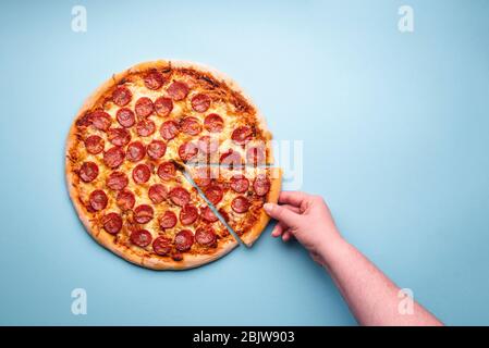 Mano della donna che afferra una fetta di pizza ai peperoni. Deliziosa pizza fatta in casa con un'abbondanza di carne. Salame a fette di pizza, vista dall'alto Foto Stock