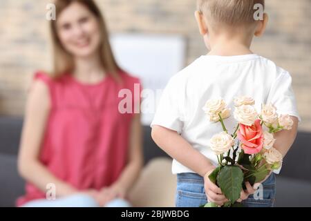 Carino ragazzino che tiene i fiori per la madre dietro la schiena, primo piano Foto Stock