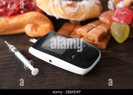 Glucometro digitale, siringa e dolci sul tavolo. Dieta per il diabete Foto Stock