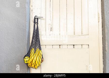 Somministrazione a domicilio durante la quarantena a causa dell'infezione da coronavirus COVID-19. Borsa con spesa con prodotti alimentari appesi sulla maniglia della porta Foto Stock