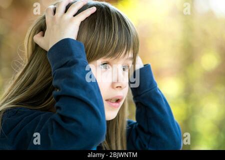 Ritratto di ragazza bambino sorpreso che tiene le mani alla sua testa all'aperto in estate. Scioccata femmina capretto in una calda giornata fuori. Foto Stock