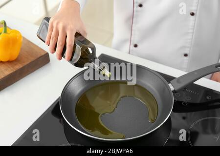 Chef che versa l'olio da cucina dalla bottiglia nella padella in stufa Foto Stock