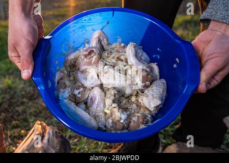 Il maschio handa contiene una ciotola blu con ali di pollo marinate. Barbecue e riposo Foto Stock