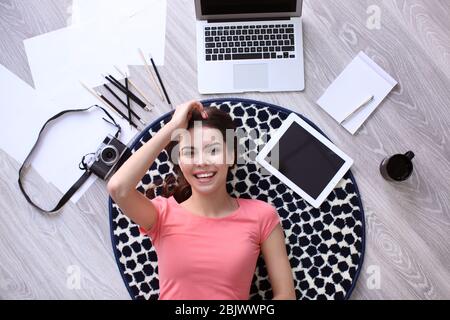 Bella giovane donna con gadget sdraiati sul pavimento, vista dall'alto Foto Stock