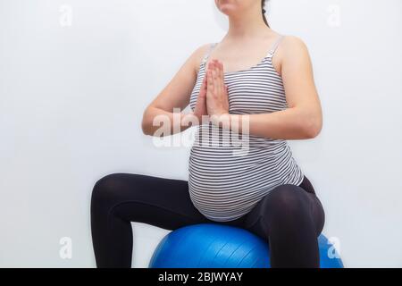 Concetto di esercizi di palla di nascita. Donna incinta irriconoscibile seduta su fittball su sfondo bianco neutro con spazio per il testo Foto Stock