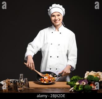 Chef femminile in cucina uniforme su sfondo scuro Foto Stock