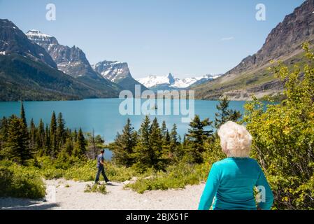 donna turistica anziana di 70 anni che guarda alle montagne, vista panoramica del lago. Godetevi la bellezza della natura al Glacier National Park. Copia sfondo spazio Foto Stock