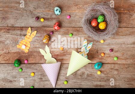 Conigli di carta, uova e caramelle su sfondo di legno. Composizione pasquale Foto Stock