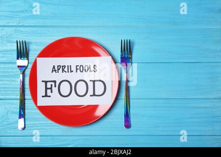 Foglio di carta con le parole 'aprile stupidi cibo', piatto e due forcelle sul tavolo Foto Stock