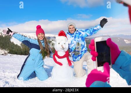 Donna fotografando i suoi amici con un pupazzo di neve presso la stazione sciistica. Vacanze invernali Foto Stock