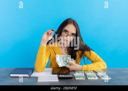 Mentre contate i soldi, una giovane donna usa una calcolatrice e un tablet per controllare la borsa valori. Foto Stock