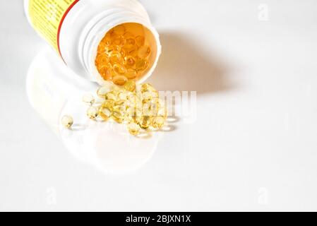 Capsule di gel giallo chiaro vitamina D3 fuoriuscite dal flacone di supplemento. Sfondo bianco con riflessione e spazio di copia Foto Stock