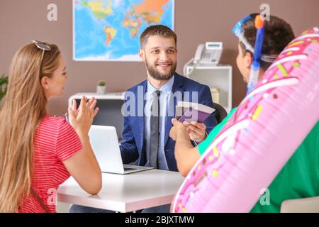 Maschio di agente di viaggi lavora con coppia giovane in office Foto Stock