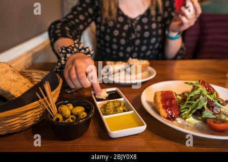 La persona femminile immerge il pane in salsa mentre mangia gli antipasti di brie e e olive cotte, aceto balsamico, olio di oliva e pesto con pane, Falkland, Fife, Foto Stock