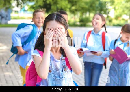 Little Schoolgirl che copre gli occhi con le mani all'aperto Foto Stock