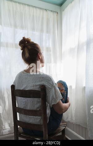 Donna seduta di fronte a finestre curced Foto Stock