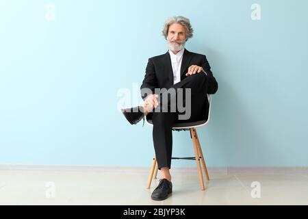 Senior alla moda uomo seduto su una sedia vicino alla parete del colore Foto Stock