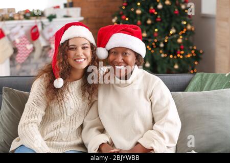 Ritratto di donna afro-americana e sua figlia in cappelli di Babbo Natale a casa Foto Stock