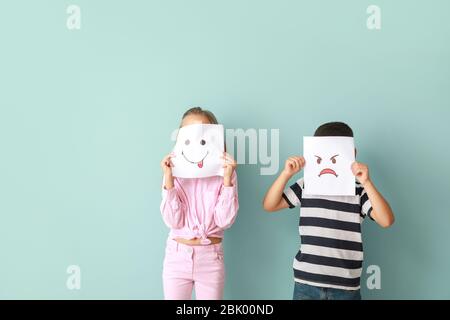 Figlioli volti nascosti dietro le emoticon disegnata sul colore di sfondo Foto Stock