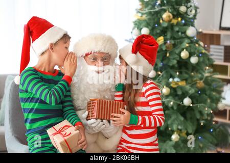 Carino piccolo bambini raccontando Santa i loro desideri in camera decorata per Natale Foto Stock