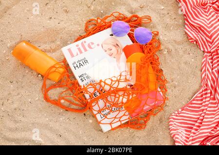 Borsa con crema di protezione solare, occhiali da sole e la rivista di moda sulla spiaggia di sabbia Foto Stock