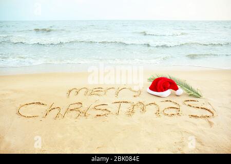 Santa Claus hat con testo scritto BUON NATALE sulla costa del mare. Vacanze di Natale Foto Stock