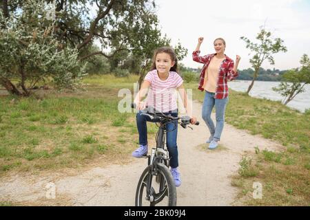 Madre orgogliosa di sua figlia che ha imparato a guidare la bicicletta all'aperto Foto Stock