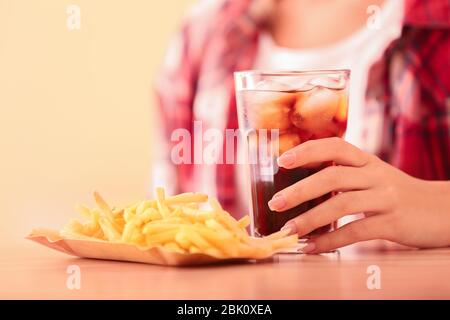 Donna con vetro a freddo cola e patatine fritte a tavola Foto Stock