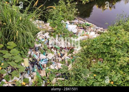 Detriti di plastica accumulati sul bordo di un fiume con acqua sporca Foto Stock