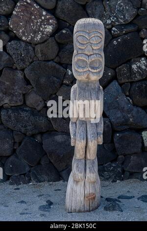 Personaggio di legno Tiki di fronte al muro di pietra lavica, il Parco storico Nazionale di pu'uhonua o Honaunau, Big Island, Hawaii Foto Stock